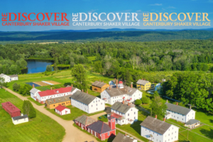 Aerial view of a colorful Shaker village with white, red, and yellow houses and green fields beneath a blue sky, with the word DISCOVER repeated across the top as a banner.
